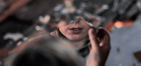 Photo of the bottom half of a woman's face reflected in a shard of mirror.