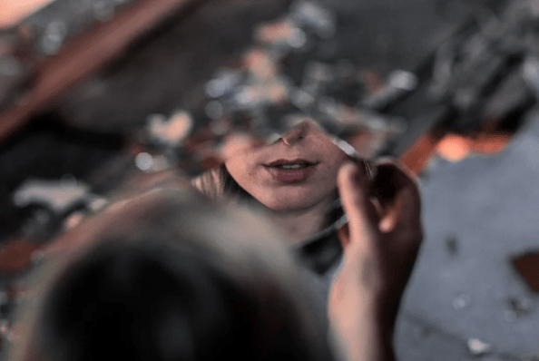 Photo of the bottom half of a woman's face reflected in a shard of mirror.